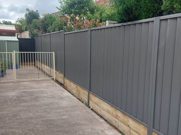 Charcoal Colorbond privacy fence on sleepers with a white garden gate in the opening