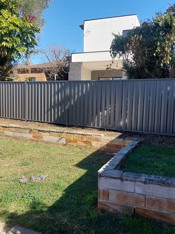 Mid grey Colorbond privacy fence above an empty garden bed on a lawn