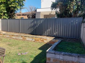 Mid grey Colorbond privacy fence above an empty garden bed on a lawn