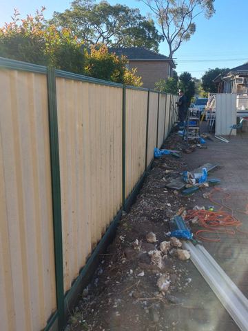 Cream Colorbond privacy fence with green posts along a building-site boundary