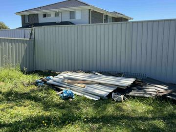 Cream Colorbond privacy fence across a lawn below a two-storey brick house