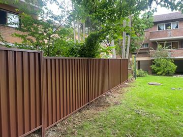 Brown Colorbond privacy fence on a lawn in front of townhouses