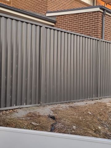 Charcoal Colorbond privacy fence in front of a brick house on a dirt yard
