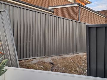Charcoal Colorbond privacy fence in front of a brick house on a dirt yard