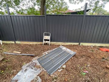 Charcoal Colorbond privacy fence on a timber sleeper across a dirt yard