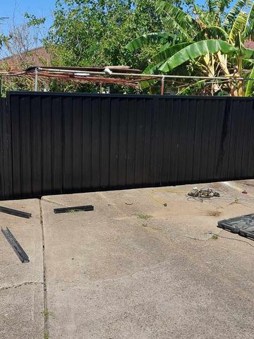 Black Colorbond privacy fence on a concrete pad with leftover hardware on the ground