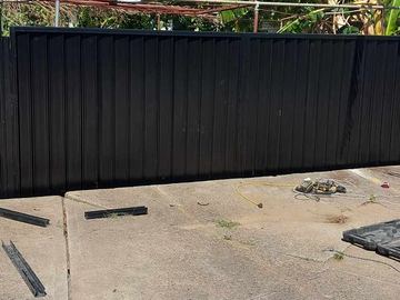 Black Colorbond privacy fence on a concrete pad with leftover hardware on the ground