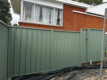 Green-grey Colorbond privacy fence in front of a two-storey brick house