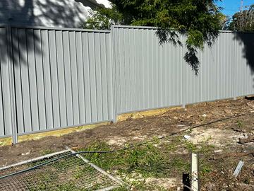 Light grey Colorbond privacy fence on a dirt yard with a leftover mesh panel