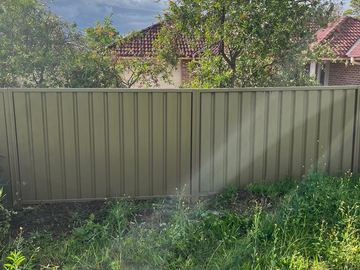 Olive Colorbond privacy fence through long grass on a backyard boundary