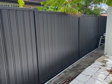 Black Colorbond privacy fence along a concrete path with a leftover rail