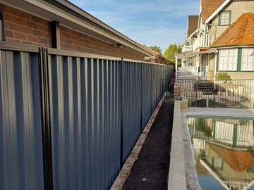 Charcoal Colorbond privacy fence running beside a narrow swimming pool