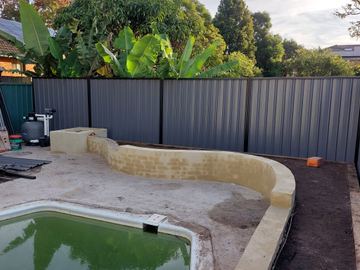 Charcoal Colorbond privacy fence around an empty concrete pool shell