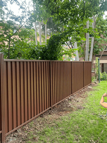 Terracotta-toned corrugated panels line a communal lawn with brick apartment buildings and overhanging trees behind.