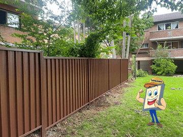 Terracotta-toned corrugated panels line a communal lawn with brick apartment buildings and overhanging trees behind.