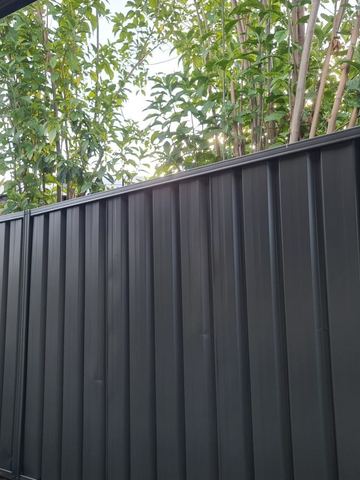 Monument corrugated panels stand before slender green trees with a red brick planter edge in the foreground.