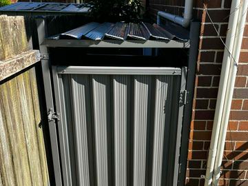 The scene shows a mid grey corrugated steel fence where sleepers form the base.