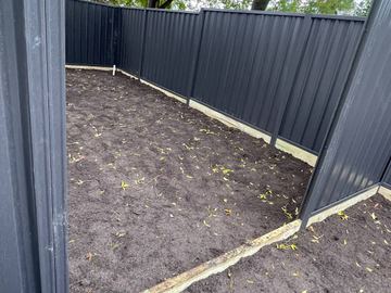 Charcoal Colorbond privacy fence enclosing a dirt backyard with a corner return