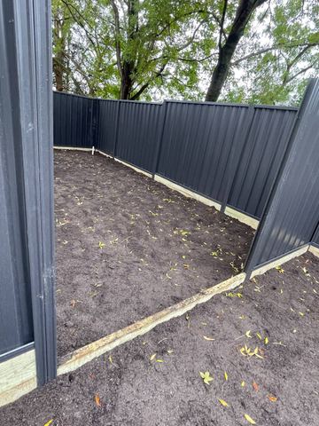 Charcoal Colorbond privacy fence enclosing a dirt backyard with a corner return