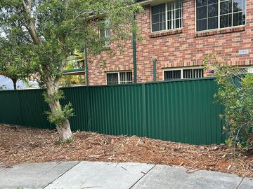 The scene shows a mid grey corrugated steel fence where sleepers form the base.