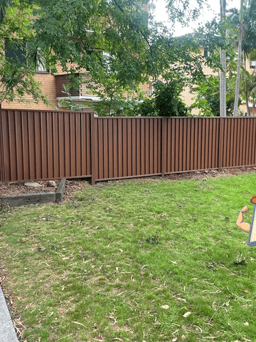 The scene shows a mid grey corrugated steel fence where garden beds sit at the base.