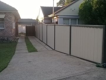 Long cream Colorbond privacy fence running along a driveway to a brick house