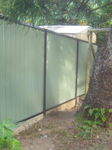 The scene shows a mid grey corrugated steel fence where sleepers form the base.