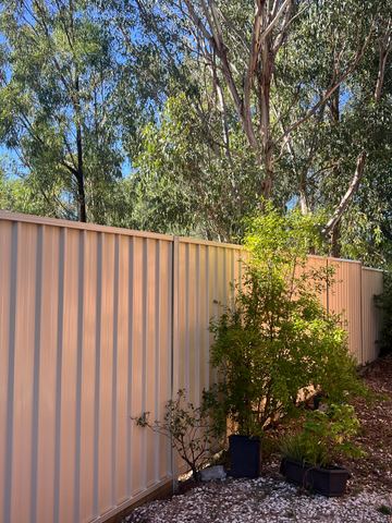 The scene shows a brown corrugated steel fence where residential buildings appear beyond the line.