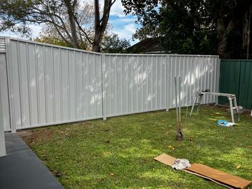 Cream Colorbond privacy fence curving across a lawn toward a neighbouring fence