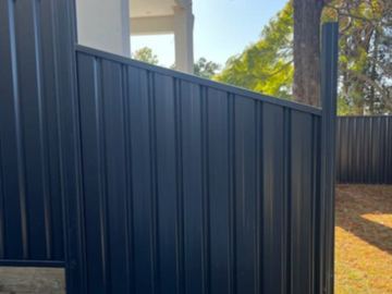 The scene shows a charcoal corrugated steel fence where sleepers form the base.