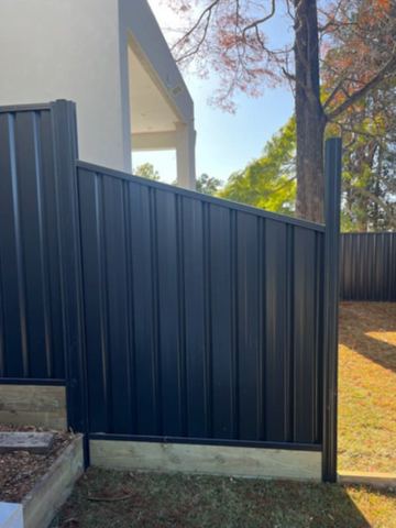 The scene shows a charcoal corrugated steel fence where sleepers form the base.