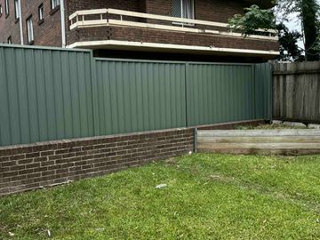 Green Colorbond privacy fence standing on a brick and timber plinth across a lawn