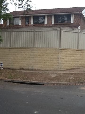 Cream Colorbond privacy fence standing on a tall block retaining wall beside a driveway