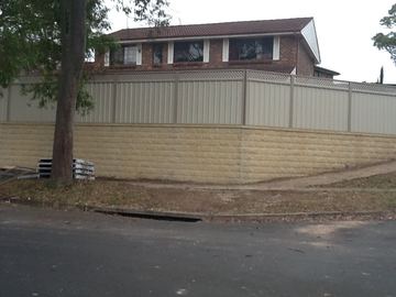 Cream Colorbond privacy fence standing on a tall block retaining wall beside a driveway