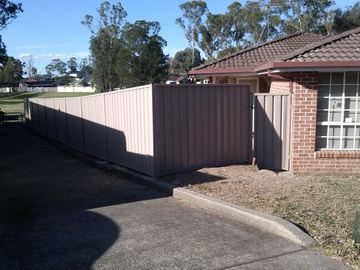Pale Colorbond privacy fence running along a driveway beside a brick house