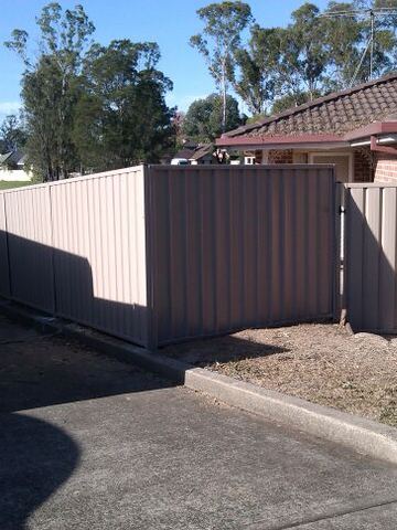 Pale Colorbond privacy fence running along a driveway beside a brick house