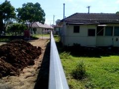 Looking along a cream Colorbond top rail toward a house across a dirt yard