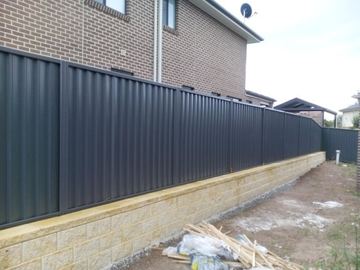 The scene shows a mid grey corrugated steel fence where sleepers form the base.