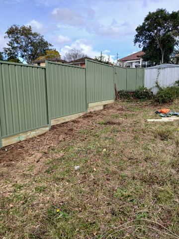 The scene shows a mid grey corrugated steel fence where sleepers form the base.