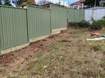 The scene shows a mid grey corrugated steel fence where sleepers form the base.