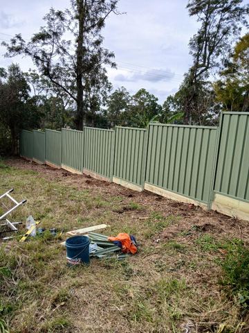 Pale green Colorbond privacy fence standing on a dirt yard with rails on the ground