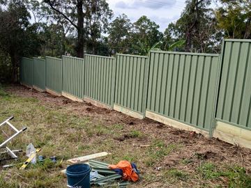 Pale green Colorbond privacy fence standing on a dirt yard with rails on the ground