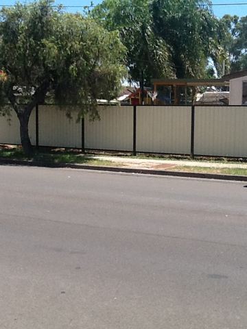 Long cream Colorbond privacy fence running along a suburban street with a parked car