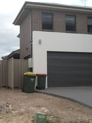Cream Colorbond pedestrian gate beside a roller-door garage on a new driveway