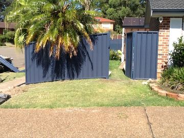Dark blue Colorbond privacy fence and matching pedestrian gate beside a brick house