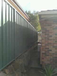 Green Colorbond privacy fence running hard against a brick house wall