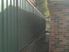 Green Colorbond privacy fence running hard against a brick house wall