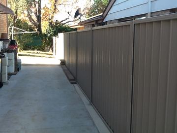 Mid grey Colorbond privacy fence running beside a concrete driveway toward a house