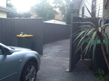 Charcoal Colorbond privacy fence beside a parked silver car and a wheelie bin