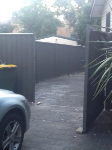 Charcoal Colorbond privacy fence beside a parked silver car and a wheelie bin